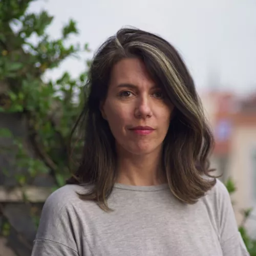 You can see a women standing. Leonor is using a grey t-shirt has a urban and green landscape on the background