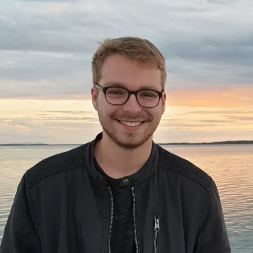 Das Bild zeigt einen lachenden Raphael Leuner vor einem See