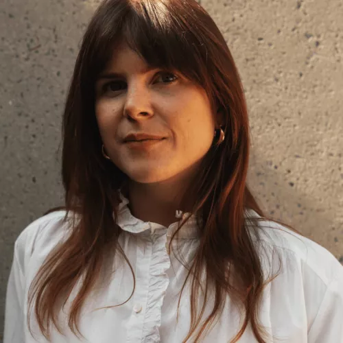 Kathy Kaenzig Portrait Image | A Woman With Brown Hair, a Fringe, And A White Blouse