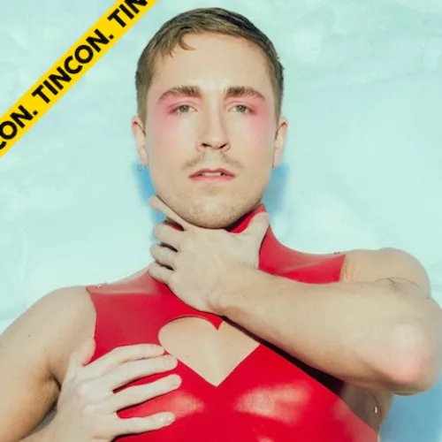 Ein Bild von Robin Solfs Oberkörper. Er hält mit einer Hand seinen Hals, mit der anderen seine Brust. Er trägt ein rotes Latex Top und schaut in die Kamera.