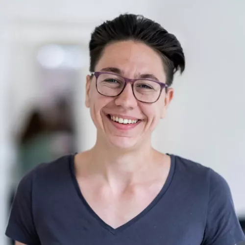 Eine Profilbild von Alexandra Wörner, einer Frau mit kurzen, braunen Haaren und Brille. Sie trägt ein dunkelgraues T-Shirt