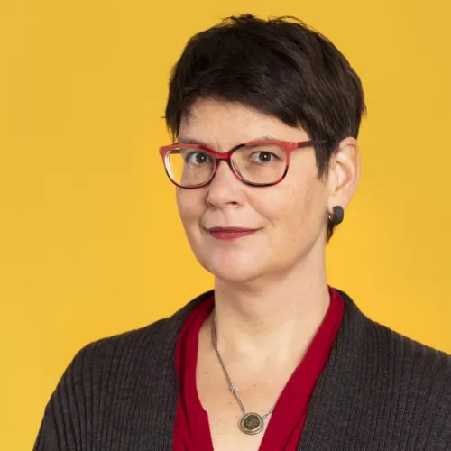 Eine Frau mittlere Alters mit kurzen braunen Haaren, braunen Augen und Brille