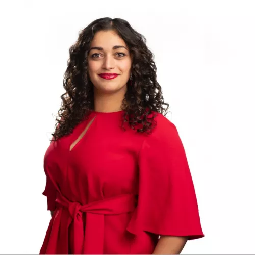 Mixed race woman with dark brown curly hair and red lipstick wearing a matching red top with cape sleeves. 