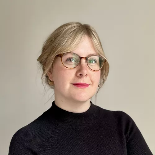 Blonde Frau mit Brille. Sie lächelt in die Kamera.