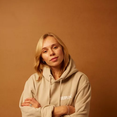 The picture is showing Ronja Lamberty wearing a hoodie with the Brand Logo WILDPLASTIC® in the front. She is positioned in a room in front of a wall. 