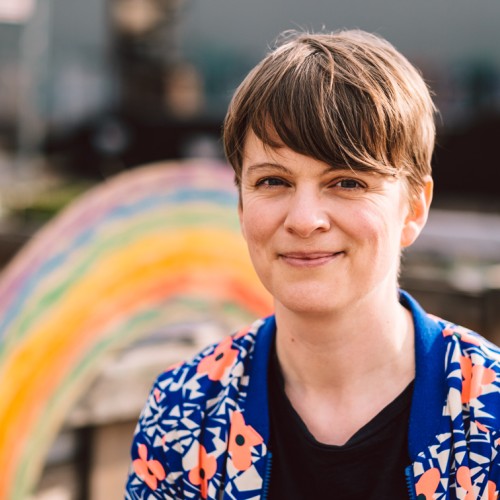 Porträt von Katrin Rönicke vor einem Holz-Regenbogen