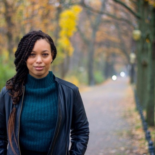 woman with individual box braids standing on a road in a park, surrounded by fall trees