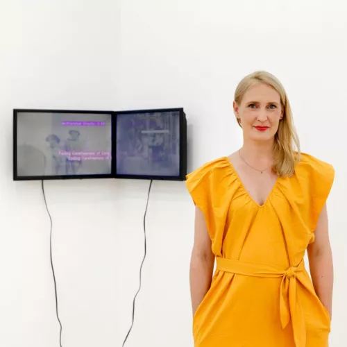 A women standing in an exhibition in front of two screens.