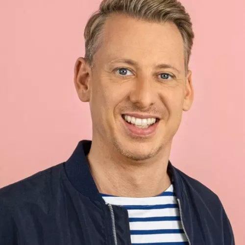 André Schünke lächelnd vor einem lachsfarbenen Hintergrund