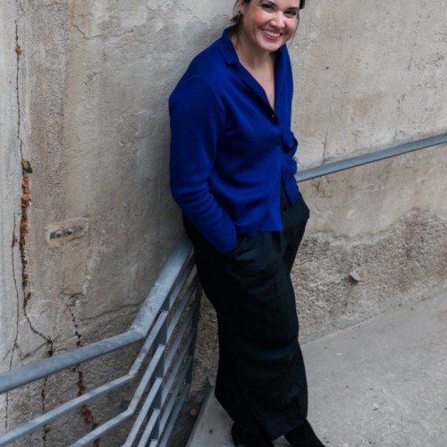 Eine Frau in blauem Hemd steht in einem Treppenabgang und lächelt.