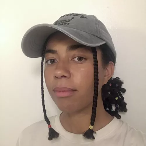 Hanna (the workshop host) wearing a white shirt and a grey hat. Her hairdo is shoulder-length braids.