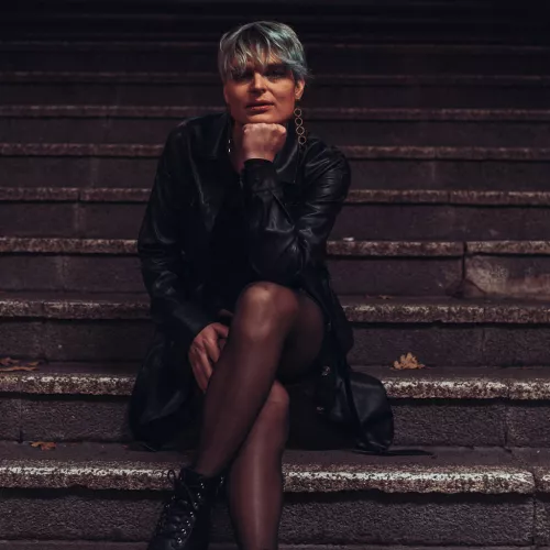 Lola Anders auf einer U-Bahn Treppe im Schwarzen Ledermantel in der Nacht 