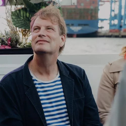 Wolfgang auf einem Boot im Hamburger Hafen in blau-weiß gestreitem Shirt und blauem Sakko.