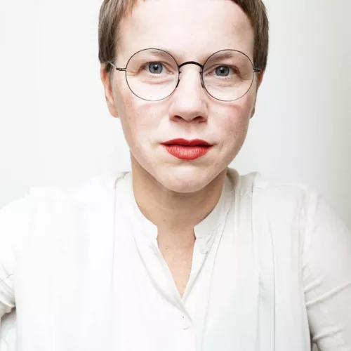 Porträt von Maiken Laackmann, kurze Haare, Brille, rote Lippen und helle Bluse