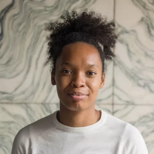 The picture shows a black woman with an afro bun wearing a white t-shirt. The background is a white marble with black wavy stripes.