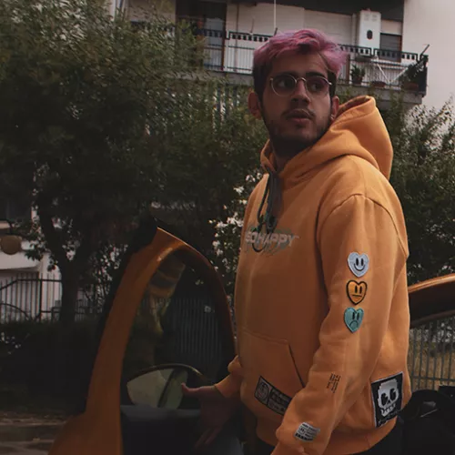 A photo of Giorgio Perri with pink hair and a yellow hoodie stepping off of a yellow car