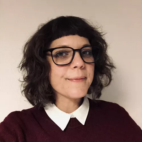 3/4 Portraitfoto einer Frau um die 40 Jahre mit Brille und schulterlangem Haar