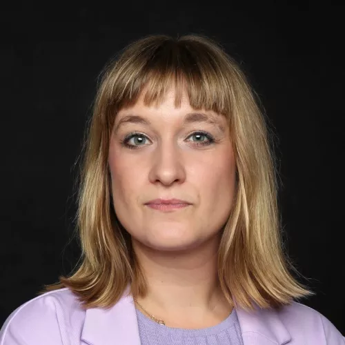 A blond woman wearing a violet jacket. 