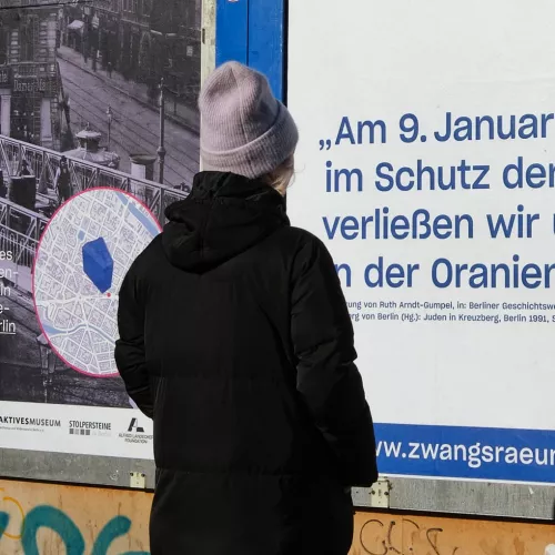 Eine Person liest ein Plakat, sie trägt einen dunklen Mantel und eine Wollmütze. 