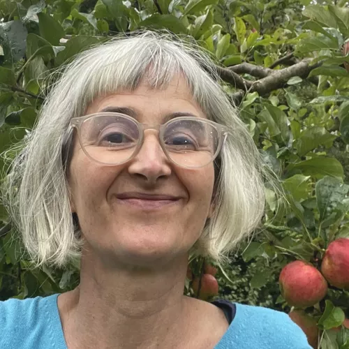 Gesicht, lächelnd, mit grauen Haaren und Brille, im Hintergrund ein Apfelbaum