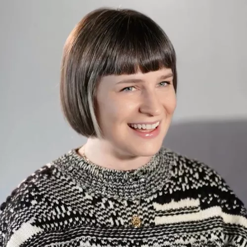 Headshot of brown haired white woman with a bob in a black and white sweater on a grey background