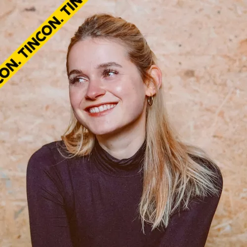Bild von Smypathisch. Sie hat halb-offene blonde Haare und ein braunes Oberteil an. Sie lächelt und guckt an der Kamera vorbei.