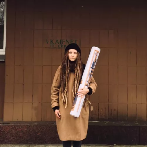 Woman in great coat and with huge rolled-up construction drawing 