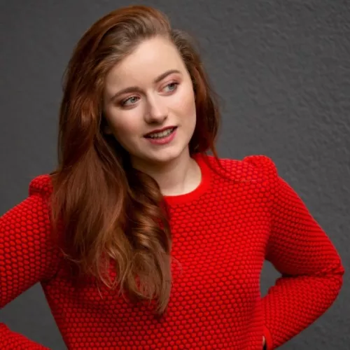 Anna Albrecht in rotem Kleid vor grauer Wand. Guckt nach rechts aus dem Bild