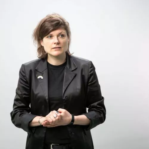Portraitfoto von Tina Lorenz, eine nonbinary Person mit halblangen Haaren, die ein Tshirt und darüber ein Jackett trägt
