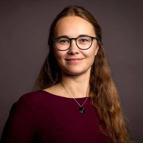 Portraitaufnahme einer Frau mit braunen Haaren und Brille vor dunklem Hintergrund