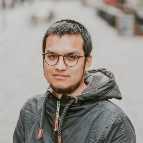Hier ist Viet Hoang zu sehen, er trägt eine grüne Kapuzenjacke und eine Brille. Er hat einen Bart.