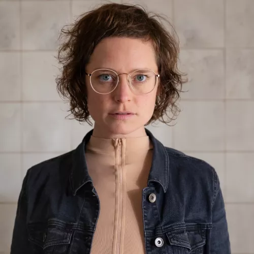 This picture shows a serious, focussed and / or slightly aggressive looking woman (Katharina Haverich) in a tiled room. 